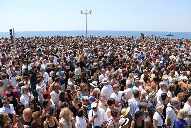 People gather to observe a minute's silence in front of the Jardin Albert 1er on the Promenade des Anglais seafront in Nice, on July 18, 2016, in tribute to the victims of the deadly Nice attack on Bastille day. France was set to hold a minute's silence on July 18, 2016 to honour the 84 victims of the Nice truck attack, but a period of national mourning was overshadowed by bickering politicians. Church bells will toll across the country, and the country will fall silent at midday, a now grimly familiar ritual after the third major terror attack in 18 months on French soil. / AFP PHOTO / Valery HACHE
