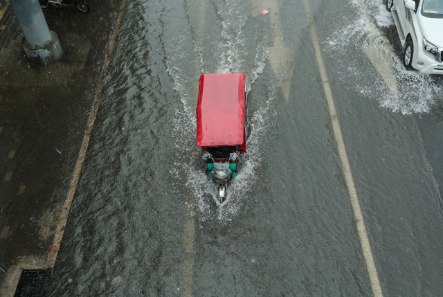 A tricycle makes its way along a flooded street in Beijing on July 20, 2016. Some areas and streets in Beijing have started to flood over due to heavy rain. / AFP PHOTO / STR