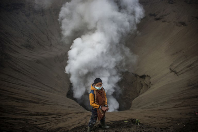 An Indonesian boy waits as he prepares to catch offerings released by Hindu devotees of the Tengger tribe during the Yadnya Kasada festival, on the crater of Mount Bromo in Probolinggo on July 21, 2016. During the annual Yadnya Kasada festival the Tenggerese climb Mount Bromo, an active volcano, and seek the blessing from the main deity Hyang Widi Wasa by presenting offerings of rice, fruit, livestock and other local produce. / AFP PHOTO / JUNI KRISWANTO