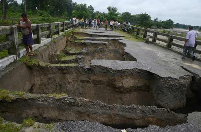 Indian people look at a bridge damaged by torrential rain at Toribari village on the outskirts of Siliguri on July 21,2016. Continuous rainfall in the past 48 hours has caused flooding with several landslides in the nearby hills of Siliguri and adjoining areas of North Bengal. / AFP PHOTO / DIPTENDU DUTTA