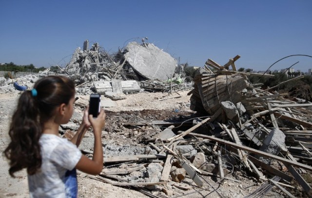 A Palestinian girl photographs the rubble of a house, that was demolished by Israeli army bulldozers, in the village of Qalandia, next to Israel's controversial separation barrier, between the Israeli occupied West Bank town of Ramallah and East Jerusalem on July 26, 2016. Israeli authorities demolished a dozen Palestinian homes in Qalandia, according to Palestinian sources. Witnesses added that shortly after midnight, a convoy of dozens of military vehicles and Israeli bulldozers stormed the resort, before demolishing 11 houses. / AFP PHOTO / AHMAD GHARABLI