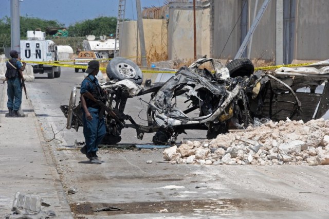 Somali soldiers pass near the wreckage of a car bomb outside the UN's office in Mogadishu on July 26, 2016. At least 13 people were killed on July 26 in twin bombings near UN and African Union buildings adjoining Mogadishu's airport, police said, in what the jihadist Shabaab group claimed as a suicide attack. / AFP PHOTO / MOHAMED ABDIWAHAB