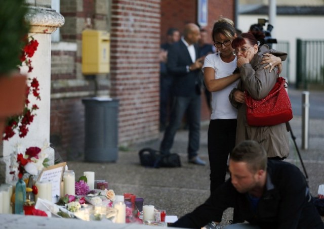 Two women react near flowers and messages displayed in front of the city hall of the Normandy city of Saint-Etienne du Rouvray on July 26, 2016 in tribute to the priest killed in the city's church in the latest of a string of attacks against Western targets claimed by or blamed on the Islamic State jihadist group. French President said that two men who attacked a church and slit the throat of a priest had "claimed to be from Daesh", using the Arabic name for the Islamic State group. Police said they killed two hostage-takers in the attack in the Normandy town of Saint-Etienne-du-Rouvray, 125 kilometres (77 miles) north of Paris. / AFP PHOTO / CHARLY TRIBALLEAU