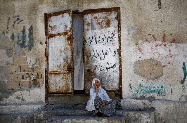 An elderly Palestinian woman sits in front of her house in Gaza City, on July 28, 2016. / AFP PHOTO / MOHAMMED ABED