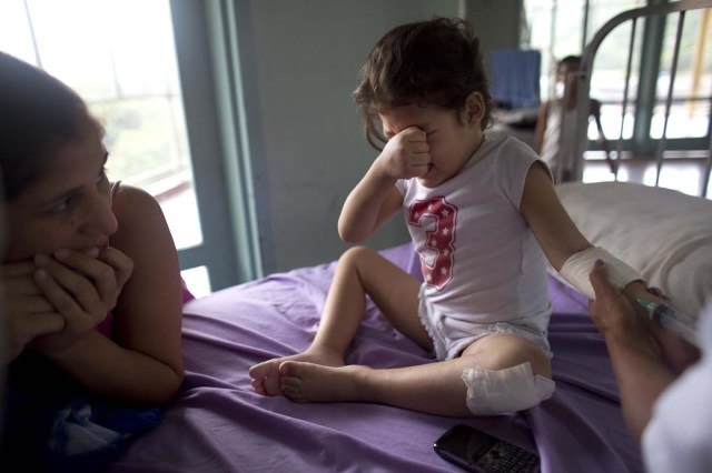 En esta imagen, tomada el 24 de agosto de 2016, Ashley Pacheco, de 3 años, llora mientras recibe una inyección ante la atenta mirada de su madre, en el hospital universitario de Caracas, Venezuela. Dos semanas después de sufrir un raspón en una rodilla, la niña se retorcía de dolor en la cama de un hospital. Le costaba respirar e imploraba a sus padres que le llevasen agua. (AP Foto/Ariana Cubillos)