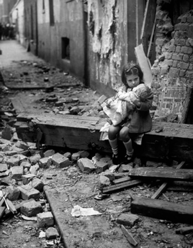 Una niña sentada entre las ruinas de su casa bombardeada abraza a su muñeca. Londres, Reino Unido, 1940.