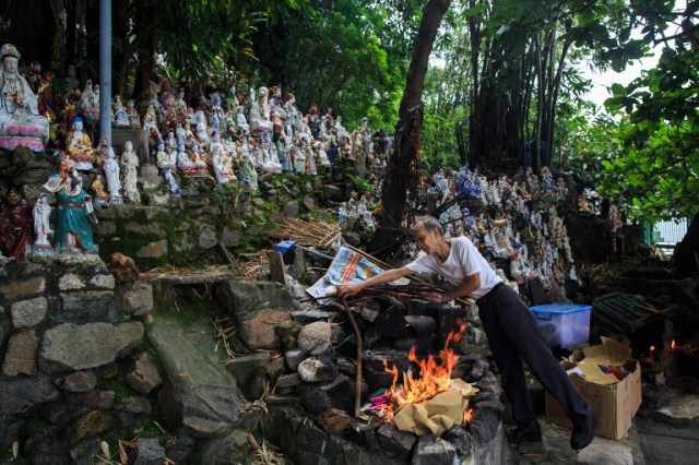 In this picture taken on August 14, 2016, dedicated volunteer Wong Wing-pong, an 85 year old retired butcher, offers 'death money' to unwanted statues of deities, gathered and repaired after their owners discarded them, on a rocky slope running down to the sea in Hong Kong, on the day of the Hungry Ghost festival. Religion and local customs permeate Hong Kong, where Buddhist and Taoist temples are common and incense offerings are regularly burned outside local businesses. Private homes often have a shrine to a local deity, with Christian churches and mosques also in the mix. But with space at a premium in a city were rents are sky high, informal collections of discarded gods often decorate roadsides and public spaces. / AFP PHOTO / Anthony WALLACE / To go with "HONG KONG-CULTURE-LIFESTYLE-RELIGION", FEATURE by Dennis Chong