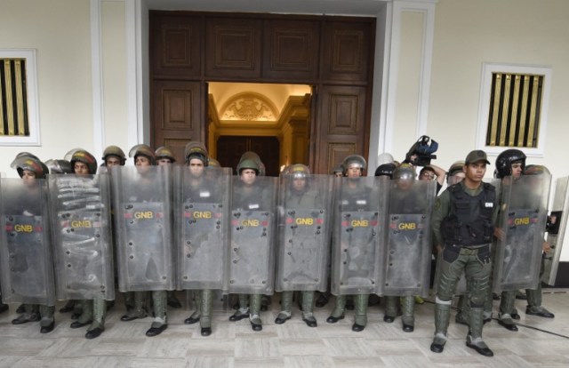 Members of the National Guard secure the entrance to the National Assembly while pro-government supporters attempt to force their way in, during an extraordinary session called by opposition leaders, in Caracas on October 23, 2016. The opposition Democratic Unity Movement (MUD) called a Parliamentary session to debate putting President Nicolas Maduro on trial to "restore democracy" in an emergency session that descended into chaos as supporters of the leftist leader briefly seized the chamber. / AFP PHOTO / JUAN BARRETO