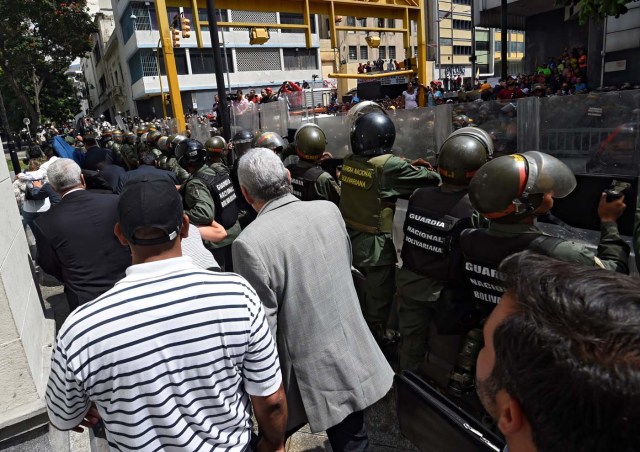 Opposition lawmakers protect themselves while they try to reach the National Assembly in Caracas on October 27, 2016. "We are going to notify Nicolas Maduro that the Venezuelan people declare he has abandoned his post," the speaker of the National Assembly, Henry Ramos Allup, said to cheers from hordes of protesters in Caracas. / AFP PHOTO / JUAN BARRETO