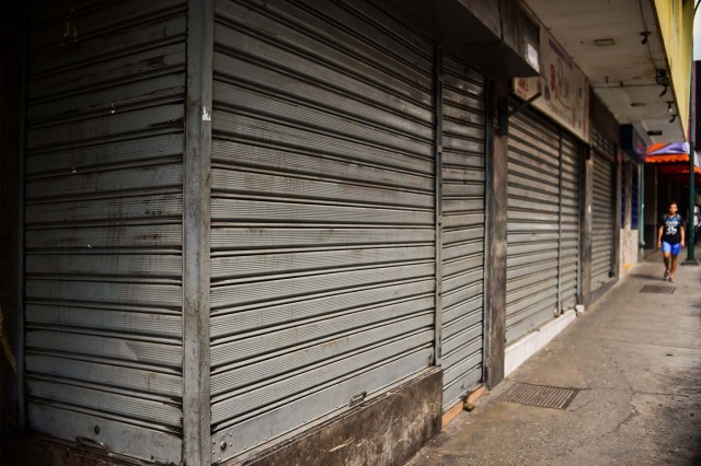 A woman walks by closed stores in Caracas, on October 28, 2016. Venezuela's opposition sought to pressure President Nicolas Maduro on Friday with a strike, which he threatened to break with army takeovers of paralyzed firms. The strike risks exacerbating the shortages of food and goods gripping the country, but it seemed to be only partially observed on Friday morning. / AFP PHOTO / RONALDO SCHEMIDT