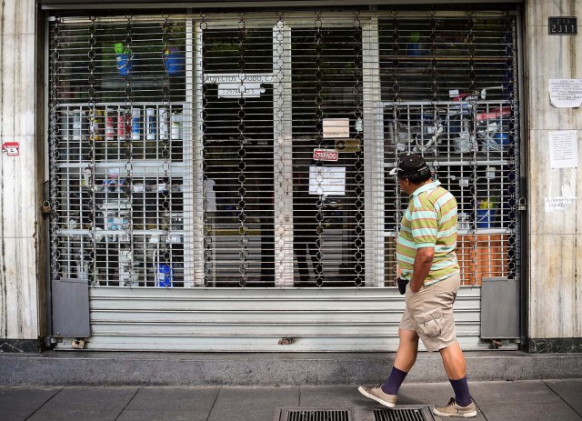 A man passes by a closed store in Caracas, on October 28, 2016. Venezuela's opposition sought to pressure President Nicolas Maduro on Friday with a strike, which he threatened to break with army takeovers of paralyzed firms. The strike risks exacerbating the shortages of food and goods gripping the country, but it seemed to be only partially observed on Friday morning. / AFP PHOTO / RONALDO SCHEMIDT