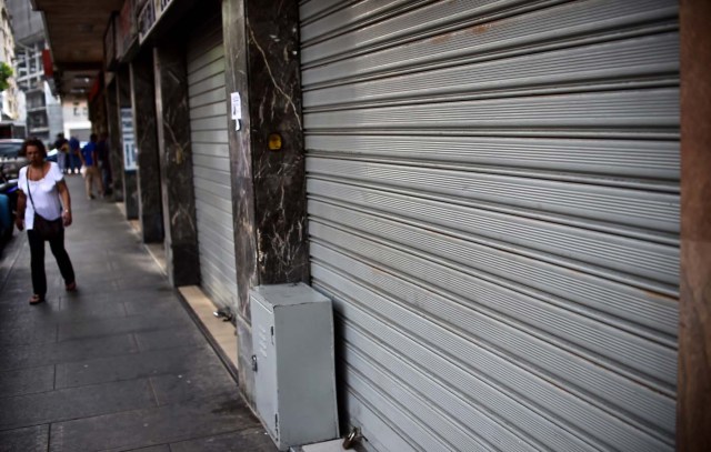 A woman walks by a closed store in Caracas, on October 28, 2016. Venezuela's opposition sought to pressure President Nicolas Maduro on Friday with a strike, which he threatened to break with army takeovers of paralyzed firms. The strike risks exacerbating the shortages of food and goods gripping the country, but it seemed to be only partially observed on Friday morning. / AFP PHOTO / RONALDO SCHEMIDT
