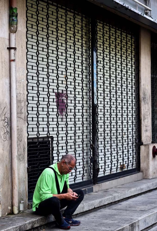 A man sits next to a closed store in Caracas, on October 28, 2016. Venezuela's opposition sought to pressure President Nicolas Maduro on Friday with a strike, which he threatened to break with army takeovers of paralyzed firms. The strike risks exacerbating the shortages of food and goods gripping the country, but it seemed to be only partially observed on Friday morning. / AFP PHOTO / RONALDO SCHEMIDT