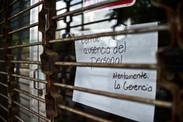 A closed store shows a sign which reads "closed for lack of staff" in Caracas, on October 28, 2016. Venezuela's opposition sought to pressure President Nicolas Maduro on Friday with a strike, which he threatened to break with army takeovers of paralyzed firms. The strike risks exacerbating the shortages of food and goods gripping the country, but it seemed to be only partially observed on Friday morning. / AFP PHOTO / RONALDO SCHEMIDT