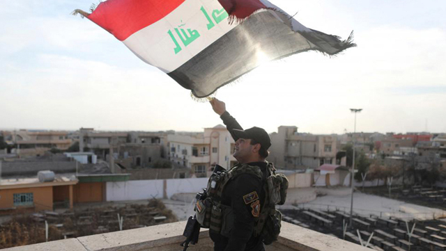Un soldado de las Fuerzas Especiales de Irak onda una bandera iraquí desde la terraza de una iglesia afectada por los combates con el EI en Bartella.