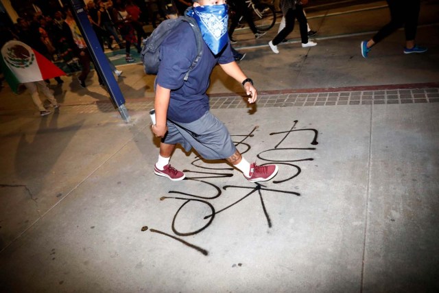 A demonstrator walks after spraying graffiti against Donald Trump on the sidewalk during a protest through the streets of downtown Los Angeles in protest following the election of Republican Donald Trump as President of the United States in Los Angeles, California November 10, 2016. REUTERS/Patrick T. Fallon TEMPLATE OUT