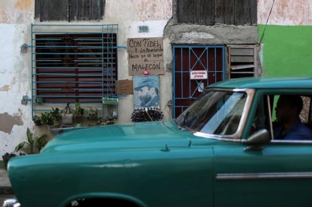 A man drives a vintage car as he passes by an image of Fidel Castro in downtown Havana, Cuba, November 27, 2016. The sign reads: "With Fidel and the Revolution until the Malecon gets dry." REUTERS/Alexandre Meneghini