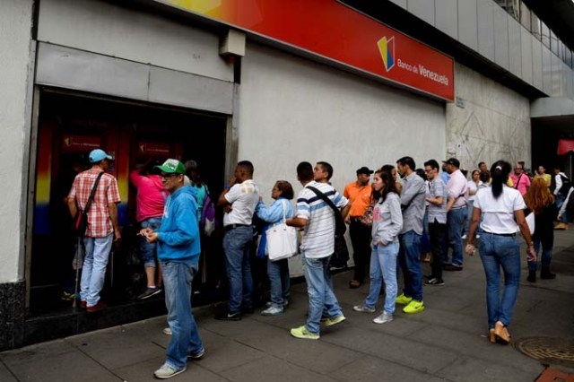 People queue to withdraw money from an automated teller machine (ATM) in Caracas on December 1, 2016. Venezuelan banks guaranteed their continued operation, after rumors about a close in December to adjust to an alleged issuance of bills of higher denomination. At the moment, the note of highest denomination is the one of 100 bolivars, that is just enough to buy a sweet. / AFP PHOTO / Federico PARRA