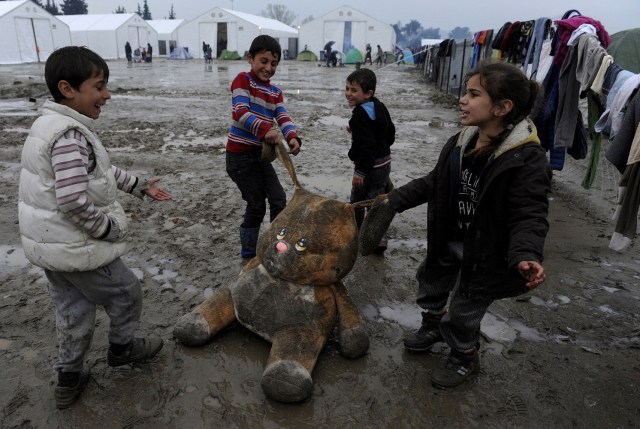 FILE PHOTO - Refugee children play with a stuffed toy at a muddy makeshift camp at the Greek-Macedonian border, near the village of Idomeni, Greece March 15, 2016. REUTERS/Alexandros Avramidis/File Photo REUTERS PICTURES OF THE YEAR 2016 - SEARCH 'POY 2016' TO FIND ALL IMAGES