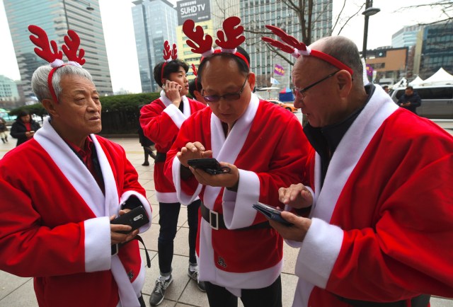 South Korean volunteers in Santa Claus outfits use their smartphones before heading out to distribute Christmas gifts at homes for prematurely born babies in Seoul on December 8, 2016. The volunteers will visit some 40 homes raising prematurely born babies in Seoul and the surrounding Gyeonggi Province. / AFP PHOTO / JUNG Yeon-Je