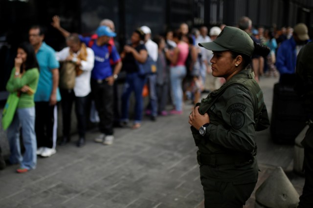 A Venezuelan soldier stands guard as people line up to get into a Banco Mercantil branch in Caracas, Venezuela December 13, 2016. REUTERS/Marco Bello