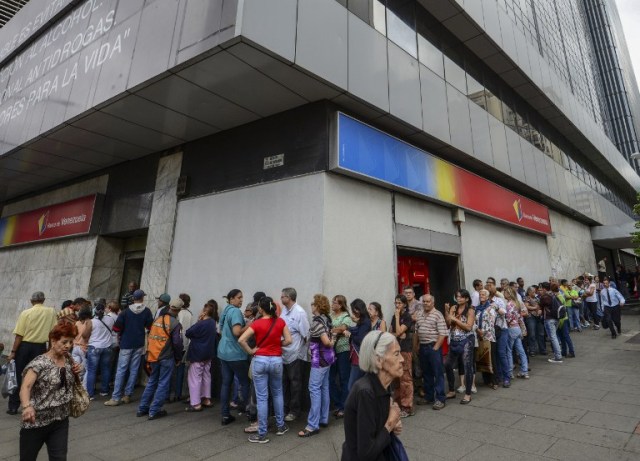 People queue outside a bank in Caracas in an attempt to deposit money, on December 13, 2016. Venezuelan President Nicolas Maduro ordered on December 12 the border with Colombia sealed for 72 hours, accusing US-backed "mafias" of conspiring to destabilize his country's economy by hoarding bank notes. The closure came a day after Maduro signed an emergency decree removing Venezuela's largest bank note, the 100 bolivar bill, from circulation because of what he called a Washington-sponsored plot against his country's troubled economy. / AFP PHOTO / JUAN BARRETO