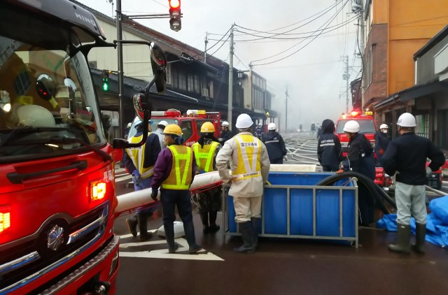 Local residents look at firefighters at the scene of a blaze that engulfed multiple buildings at Itoigawa city, Niigata prefecture on December 22, 2016.         A rapidly-spreading fire engulfed more than 100 buildings and sparked evacuations in a northern Japanese city on December 22, leaving two injured and forcing authorities to mobilise troops. / AFP PHOTO / JIJI PRESS / JIJI PRESS / Japan OUT