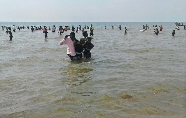 People help a man to come ashore from Lake Albert, on December 26, 2016 in Buliisa, after at least 30 Ugandan members of a village football team and their fans drowned when their boat capsized on Lake Albert during a party. Police officers working with local fishermen managed to rescue 15 of the revellers, who were heading from the village of Kaweibanda in the western Buliisa District to watch a friendly Christmas Day match in Hoima District, Rutagira said. / AFP PHOTO / -