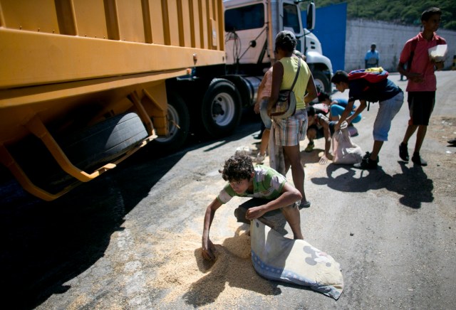 En esta imagen del 14 de noviembre de 2016, un joven utiliza una funda de almohada para recoger arroz del pavimento caído de un camión de mercancías que espera para entrar en Puerto Cabello, Venezuela. (AP Foto/Ariana Cubillos)