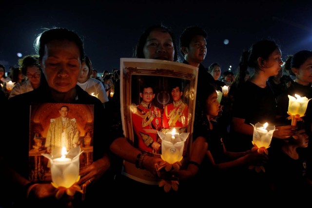 Well-wishers hold up picture of Thailand's new King Maha Vajiralongkorn Bodindradebayavarangkun and late King Bhumibol Adulyadej and candle lights as they pray to celebrate the new year at Sanam Luang park in Bangkok, Thailand January 1, 2017. REUTERS/Chaiwat Subprasom