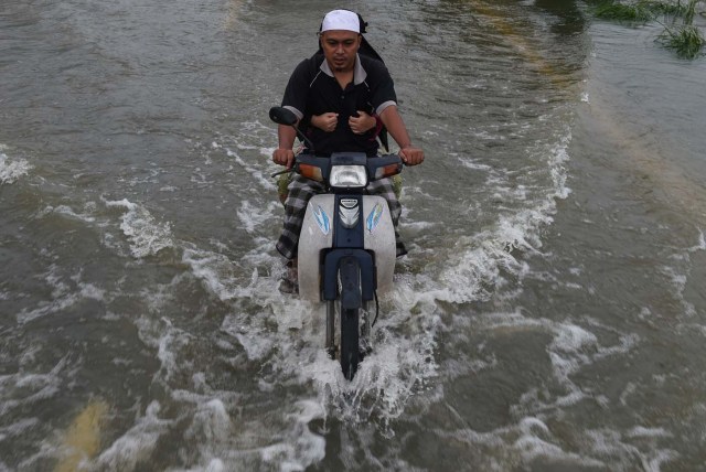 A local resident rides a motorcycle with his wife through floodwaters in Jal Besar, Malaysia's northeastern town of Tumpat, which borders Thailand on January 6, 2017. Floods continued to inundate two northeast Malaysian states, as thousands of people remained in relief centres while others expressed fears of looting and sought aid. / AFP PHOTO / MOHD RASFAN