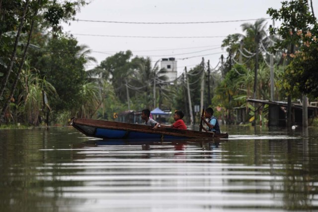 Boys travel by boat through floodwaters in Jal Besar, Malaysia's northeastern town of Tumpat, which borders with Thailand, on January 6, 2017. Serious flooding in Malaysia's northeast states for almost a week is showing some respite but has damaged homes, caused loss of income and disrupted schooling, victims said on January 6. / AFP PHOTO / Mohd RASFAN