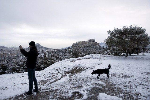 A man takes a photo of the snowy cityscape from atop the Pnyka hill as the ancient Parthenon temple is seen atop the Acropolis hill following a snowfall in Athens, Greece, January 10, 2017. REUTERS/Alkis Konstantinidis