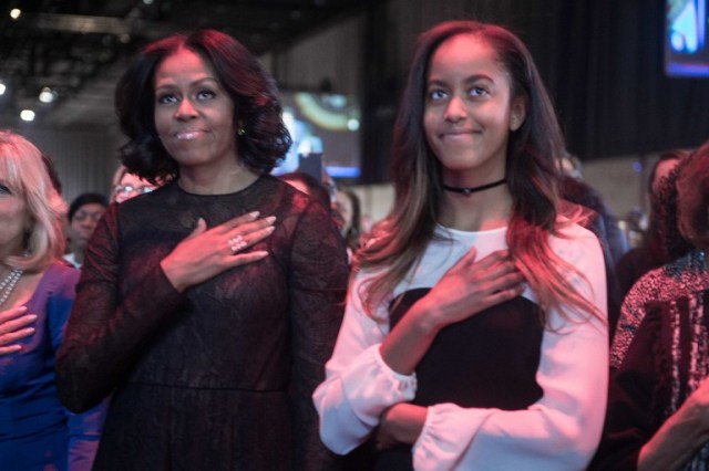 US First Lady Michelle Obama (L) and daughter Malia listen to the national anthem before President Barack Obama delivered his farewell address in Chicago, Illinois on January 10, 2017. Barack Obama closes the book on his presidency, with a farewell speech in Chicago that will try to lift supporters shaken by Donald Trump's shock election. / AFP PHOTO / NICHOLAS KAMM