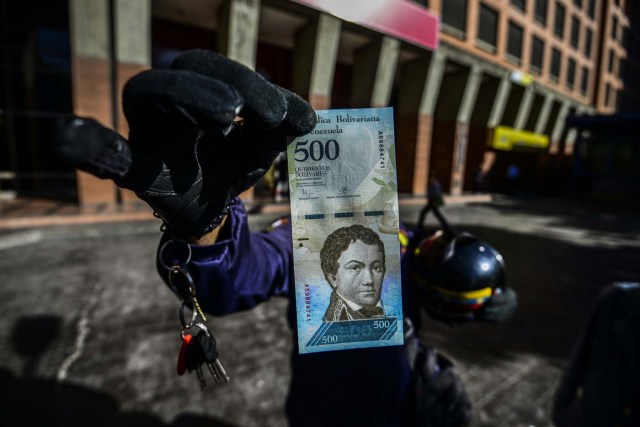 A man shows a new 500-Bolivar-note (74 cents of US dollar) in Caracas on January 16, 2017. A new family of currency will progressively come into circulation in the South American country that has the highest inflation rate in the world, which IMF forecasts say could soon hit 475 percent. / AFP PHOTO / JUAN BARRETO