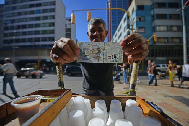 A street coffee vendor shows a new 500-Bolivar-note (74 cents of US dollar) in Caracas on January 16, 2017. A new family of currency will progressively come into circulation in the South American country that has the highest inflation rate in the world, which IMF forecasts say could soon hit 475 percent. / AFP PHOTO / JUAN BARRETO