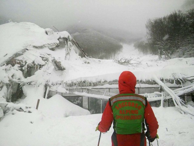 A member of Lazio's Alpine and Speleological Rescue Team stands in front of the Hotel Rigopiano in Farindola, central Italy, hit by an avalanche, in this January 19, 2017 handout picture provided by Lazio's Alpine and Speleological Rescue Team. Soccorso Alpino Speleologico Lazio/Handout via REUTERS ATTENTION EDITORS - THIS IMAGE WAS PROVIDED BY A THIRD PARTY. IT WAS PROCESSED BY REUTERS TO ENHANCE QUALITY. AN UNPROCESSED VERSION HAS BEEN PROVIDED SEPARATELY. EDITORIAL USE ONLY. NO RESALES. NO ARCHIVE. TPX IMAGES OF THE DAY