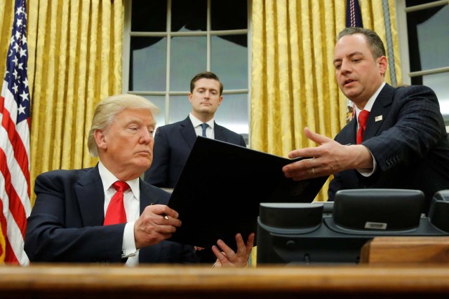 U.S. President Donald Trump hands Chief of Staff Reince Priebus (R) an executive order that directs agencies to ease the burden of Obamacare, after signing it in the Oval Office in Washington, U.S. January 20, 2017. Also pictured is White House Staff Secretary Rob Porter (C). REUTERS/Jonathan Ernst TPX IMAGES OF THE DAY