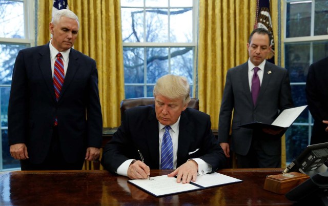 U.S. President Donald Trump signs an executive order on U.S. withdrawal from the Trans Pacific Partnership while flanked by Vice President Mike Pence (L) and White House Chief of Staff Reince Priebus (R) in the Oval Office of the White House in Washington January 23, 2017.   REUTERS/Kevin Lamarque