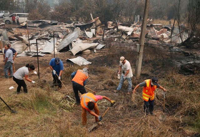 Residents clear the vegetation next to remains of a burned down public school, while wildfires ravaged wide swaths of the country's central-south regions, in town of Hualqui