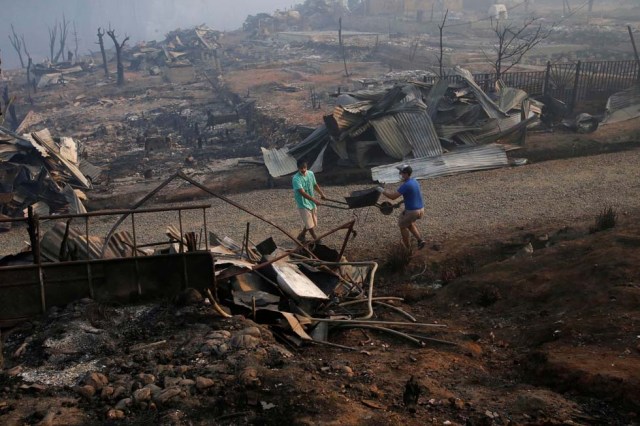 People carry a wheelbarrow among the remains of burnt houses after a wildfire at the country's central-south regions, in Santa Olga