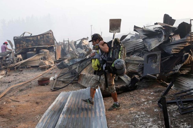 A man walks among the remains of burnt houses after a wildfire at the country's central-south regions in Santa Olga