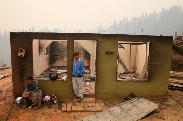 People stay at the remains of a burnt house after a wildfire at the country's central-south regions, in Santa Olga,