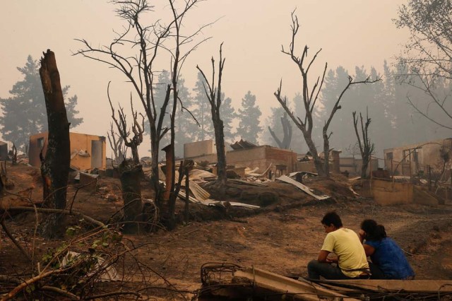 People sit near burnt houses after a wildfire in the country's central-south regions, in Santa Olga