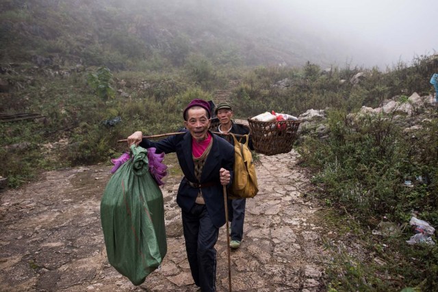 This photo taken on November 6, 2016 shows two men holding goods as they walk on the only path to reach Zhongdong village, where a group of 18 families live inside an enormous natural cave. The final hold-outs of the country's "last cave-dwelling" village have had modern conveniences, like electricity, for years. But their only access to the outside world is a footpath winding through Guizhou province's rugged mountain terrain. / AFP PHOTO / FRED DUFOUR / TO GO WITH China-economy-tourism,FEATURE by Becky Davis