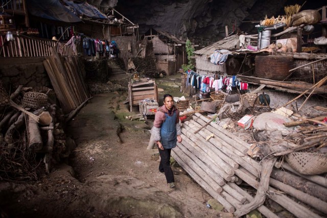 This photo taken on November 6, 2016 shows a woman walking throuh the village of Zhongdong, where a group of 18 families live inside an enormous natural cave. The final hold-outs of the country's "last cave-dwelling" village have had modern conveniences, like electricity, for years. But their only access to the outside world is a footpath winding through Guizhou province's rugged mountain terrain. / AFP PHOTO / FRED DUFOUR / TO GO WITH China-economy-tourism,FEATURE by Becky Davis