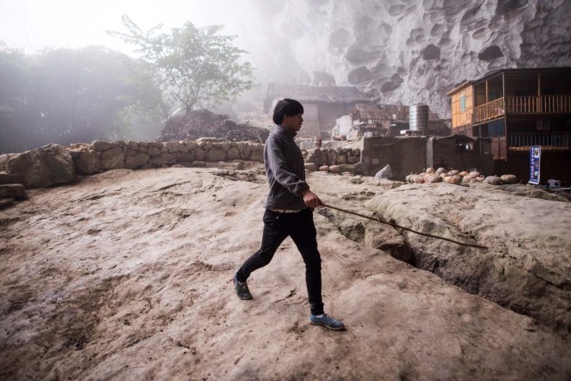 This photo taken on November 6, 2016 shows a man walks in the village of Zhongdong, where a group of 18 families live inside an enormous natural cave. The final hold-outs of the country's "last cave-dwelling" village have had modern conveniences, like electricity, for years. But their only access to the outside world is a footpath winding through Guizhou province's rugged mountain terrain. / AFP PHOTO / FRED DUFOUR / TO GO WITH China-economy-tourism,FEATURE by Becky Davis