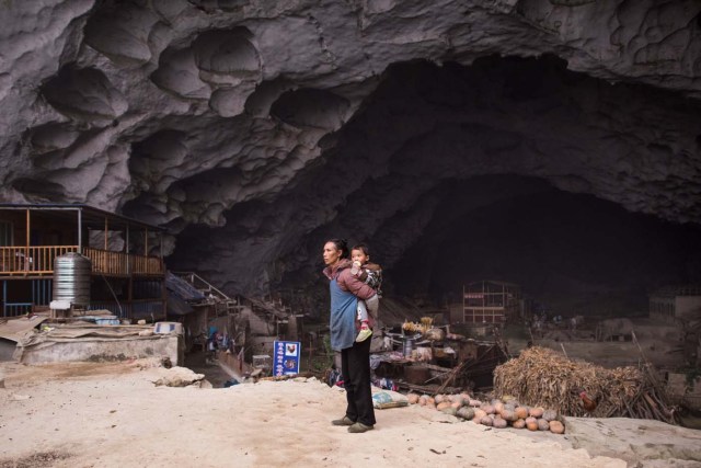 This photo taken on November 6, 2016 shows a woman holding a baby on her back in the village of Zhongdong, where a group of 18 families live inside an enormous natural cave. The final hold-outs of the country's "last cave-dwelling" village have had modern conveniences, like electricity, for years. But their only access to the outside world is a footpath winding through Guizhou province's rugged mountain terrain. / AFP PHOTO / FRED DUFOUR / TO GO WITH China-economy-tourism,FEATURE by Becky Davis