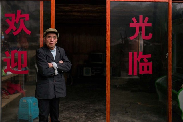 This photo taken on November 6, 2016 shows a man standing in front of the door of his shop in Zhongdong village, where a group of 18 families live inside an enormous natural cave. The final hold-outs of the country's "last cave-dwelling" village have had modern conveniences, like electricity, for years. But their only access to the outside world is a footpath winding through Guizhou province's rugged mountain terrain. / AFP PHOTO / FRED DUFOUR / TO GO WITH China-economy-tourism,FEATURE by Becky Davis