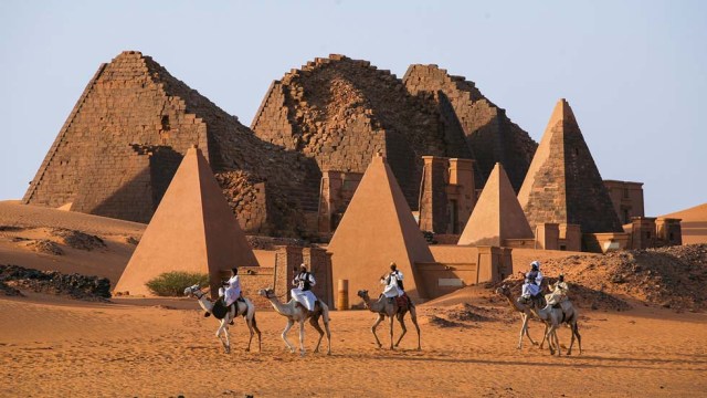 MEROE PYRAMIDS, SUDAN - NOV 02, 2007 : Unidentified Sudanese bedouins ride camels with the famous Meroe pyramids of the ancient Nubian city in the background, on November 02, 2007 in Sudan